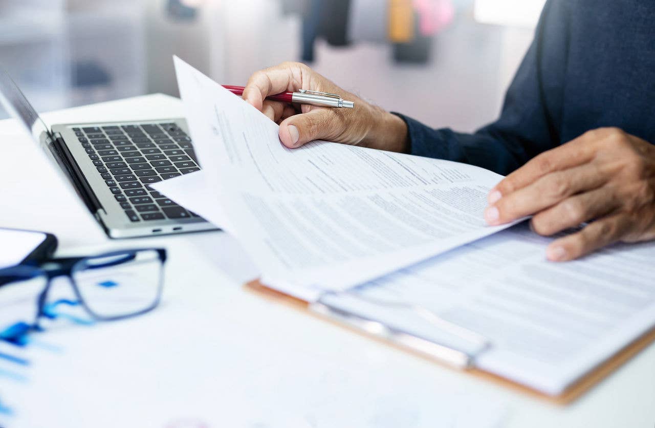 Homme consultant des documents papier à son bureau avec un ordinateur portable à côté