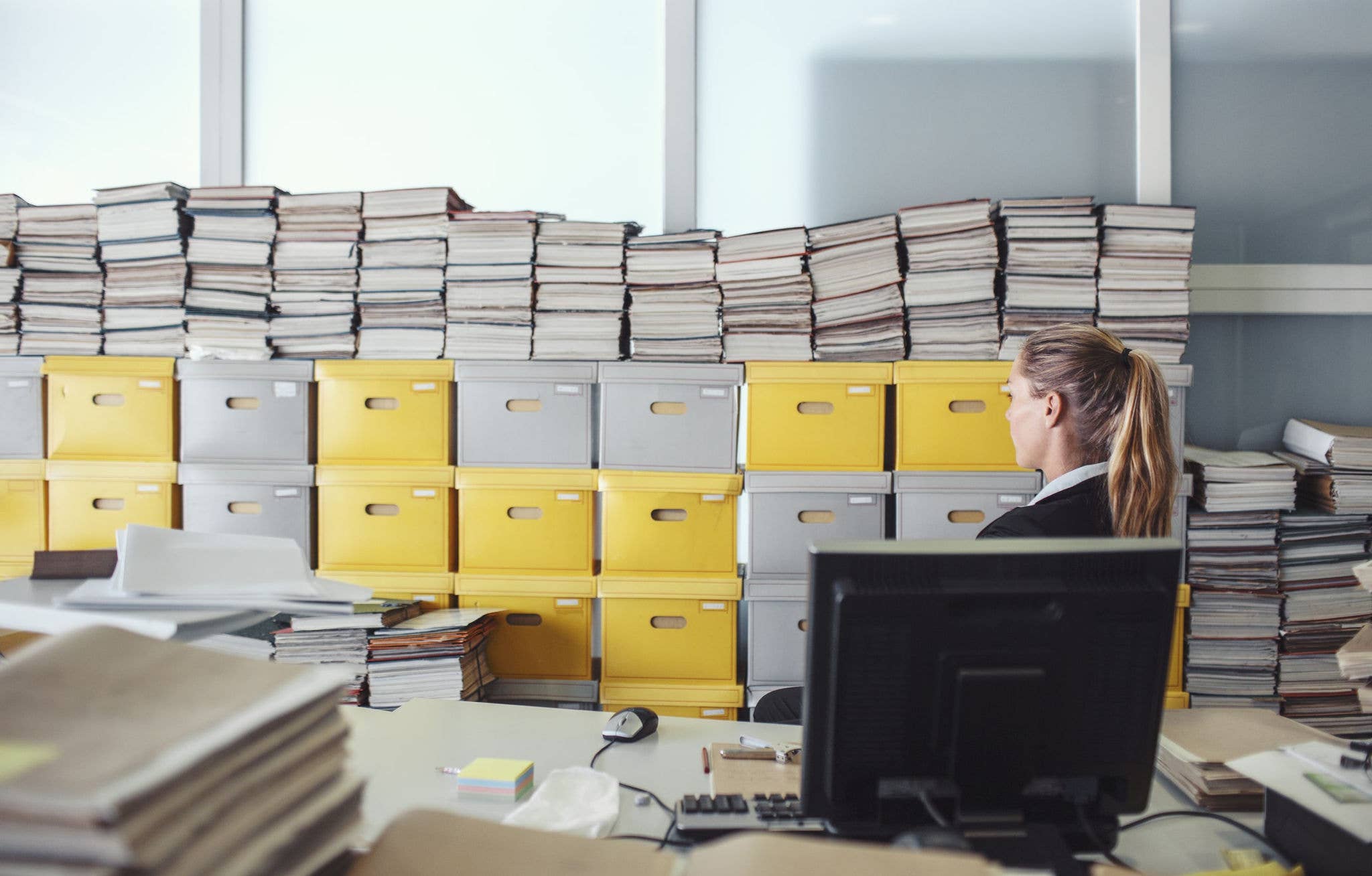 Femme assise derrière un bureau rempli d'archives